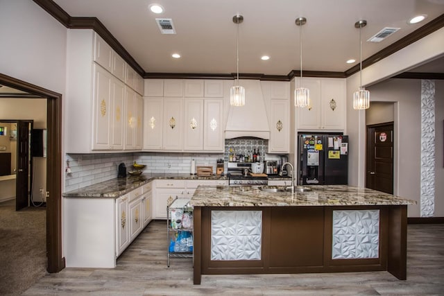 kitchen featuring premium range hood, black fridge with ice dispenser, sink, hanging light fixtures, and dark stone counters