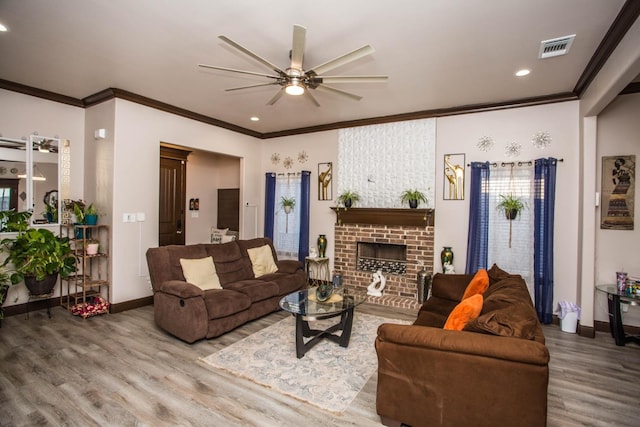 living room with wood-type flooring, a brick fireplace, ornamental molding, and ceiling fan