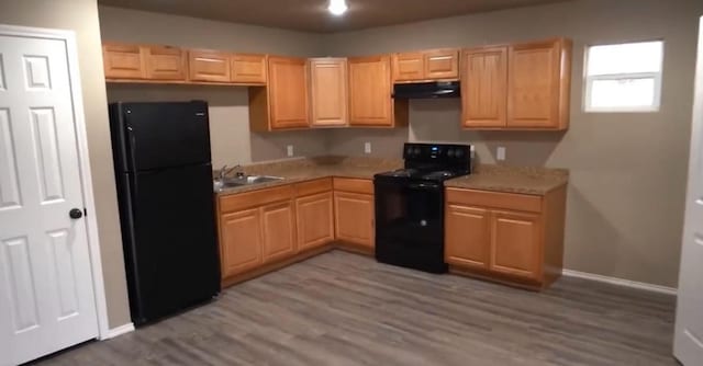 kitchen with light brown cabinetry, sink, hardwood / wood-style floors, and black appliances