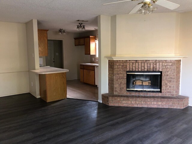 unfurnished living room with a brick fireplace, dark wood-type flooring, a textured ceiling, and ceiling fan