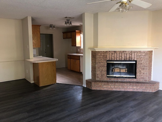 unfurnished living room featuring dark wood-type flooring, ceiling fan, a brick fireplace, and a textured ceiling