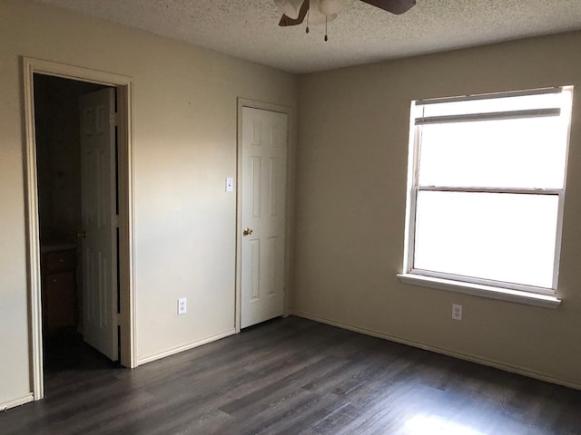 unfurnished bedroom with multiple windows, ceiling fan, dark wood-type flooring, and a textured ceiling