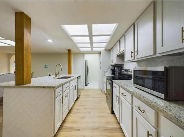 kitchen with sink, light stone counters, stainless steel appliances, light hardwood / wood-style floors, and white cabinets