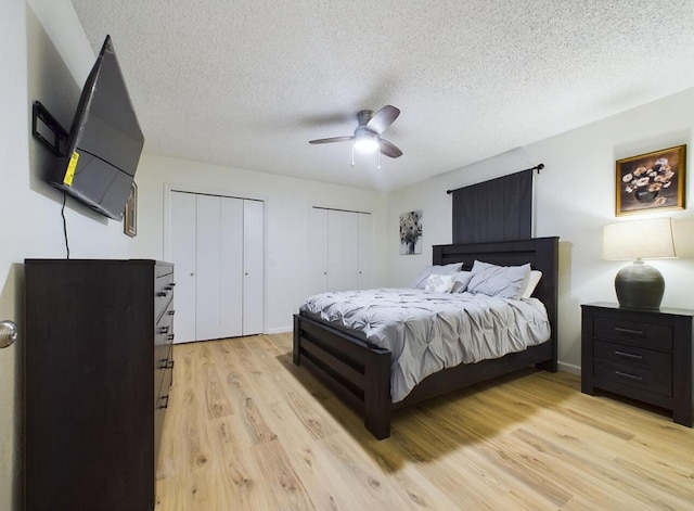 bedroom with ceiling fan, two closets, a textured ceiling, and light hardwood / wood-style flooring