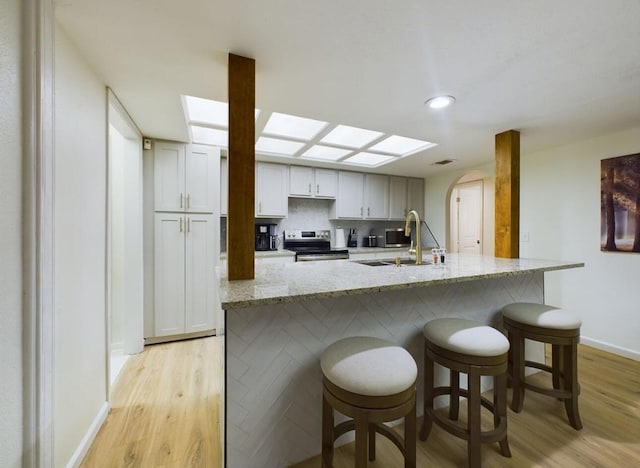 kitchen with sink, a breakfast bar area, light stone counters, light hardwood / wood-style flooring, and electric stove