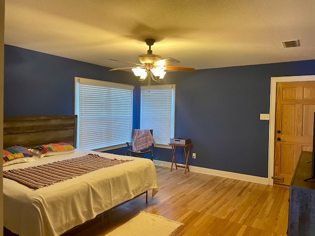 bedroom with ceiling fan, light hardwood / wood-style floors, and a textured ceiling