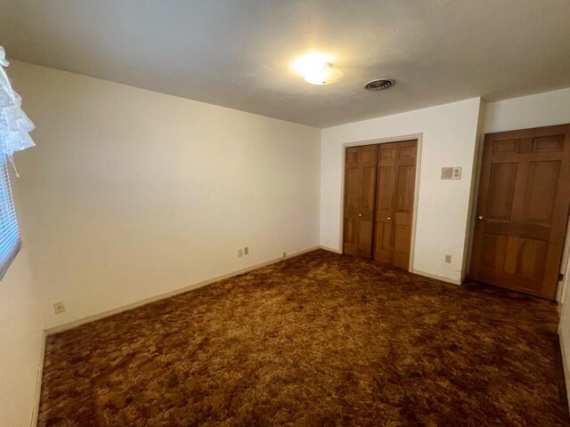 unfurnished bedroom with dark colored carpet and a closet