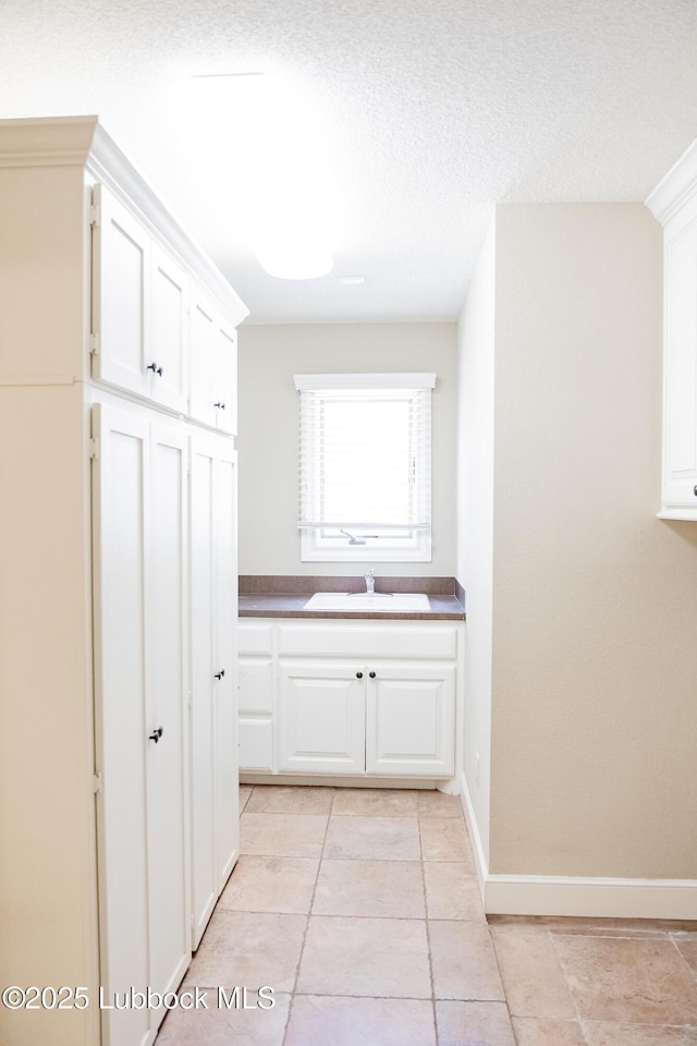 9805 Savannah Ave, Lubbock, TX 79424 - corridor with a sink, light tile patterned flooring, baseboards, and a textured ceiling
