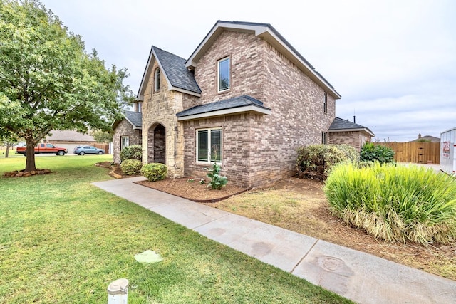 view of front facade with brick siding, stone siding, a front lawn, and fence