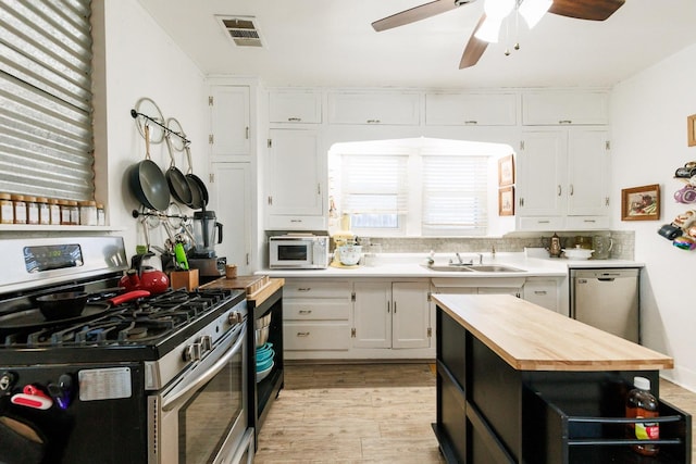 kitchen featuring sink, butcher block countertops, white cabinetry, appliances with stainless steel finishes, and light hardwood / wood-style floors