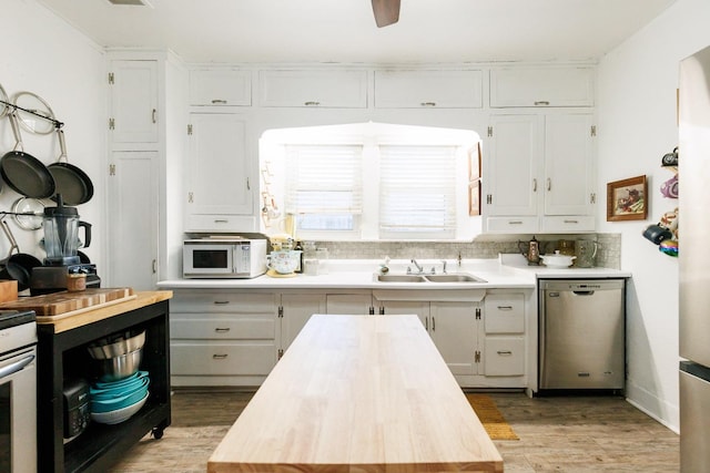 kitchen with butcher block countertops, white cabinetry, sink, decorative backsplash, and stainless steel dishwasher