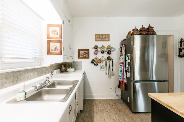 kitchen featuring sink, white cabinets, stainless steel fridge, backsplash, and light wood-type flooring