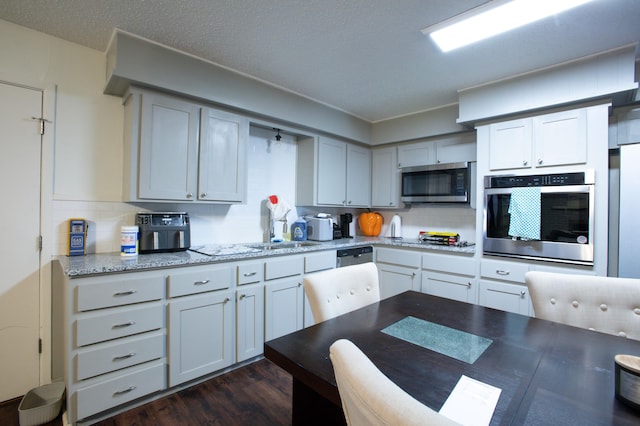 5426 9th St, Lubbock, TX 79416 - kitchen with appliances with stainless steel finishes, tasteful backsplash, dark wood-type flooring, and light stone counters