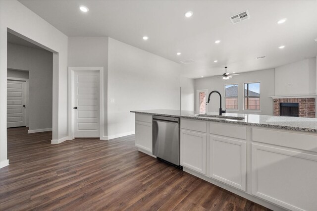 kitchen with sink, a brick fireplace, stainless steel dishwasher, light stone countertops, and white cabinets