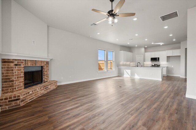 unfurnished living room featuring ceiling fan, dark hardwood / wood-style floors, sink, and a fireplace