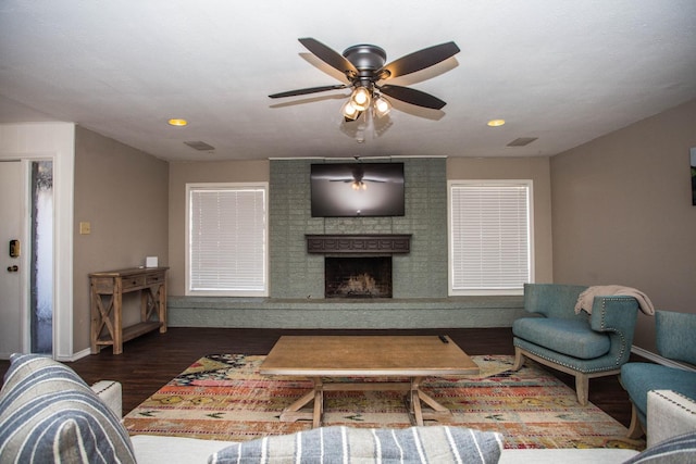 living room with a brick fireplace, dark hardwood / wood-style floors, and ceiling fan