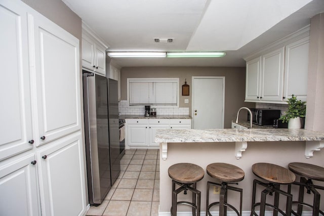 kitchen with white cabinetry, stainless steel fridge, and a kitchen bar