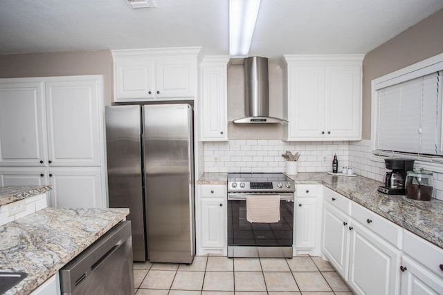 kitchen featuring wall chimney range hood, light tile patterned floors, appliances with stainless steel finishes, white cabinets, and decorative backsplash