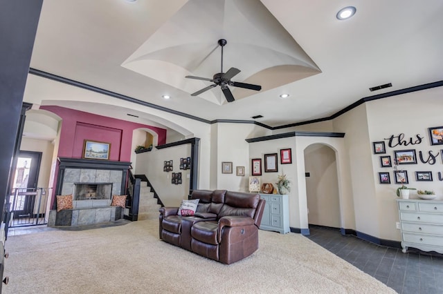 living room featuring a tile fireplace, ornamental molding, ceiling fan, and dark carpet