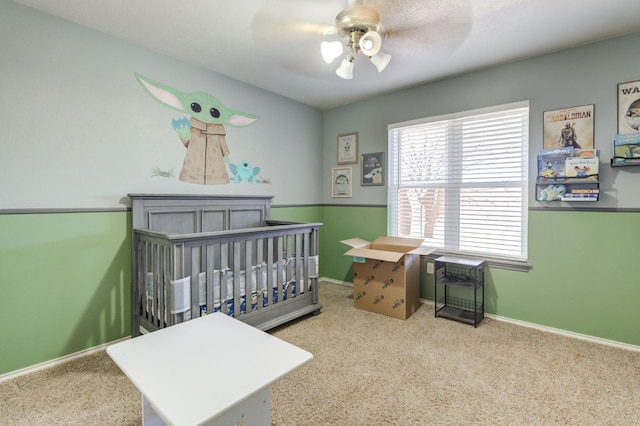 bedroom featuring a crib, light colored carpet, and ceiling fan