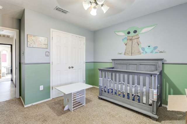 carpeted bedroom with a crib, a closet, and ceiling fan