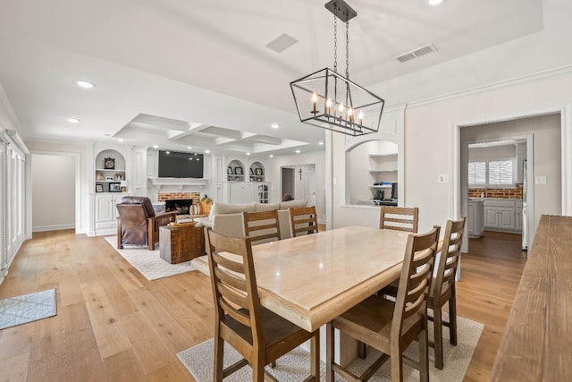 dining area with crown molding, light hardwood / wood-style flooring, built in features, coffered ceiling, and a brick fireplace