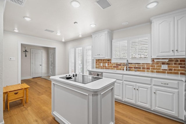 kitchen with sink, crown molding, light wood-type flooring, a kitchen island, and white cabinets