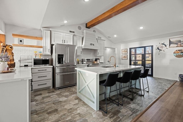 kitchen with premium range hood, a kitchen bar, sink, appliances with stainless steel finishes, and a kitchen island with sink