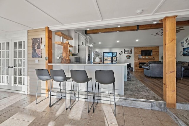 kitchen with a breakfast bar area, white cabinetry, beam ceiling, high quality fridge, and kitchen peninsula