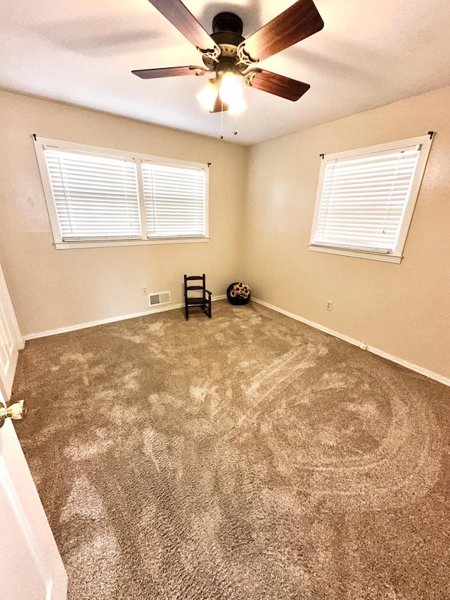 carpeted empty room featuring a ceiling fan, visible vents, and baseboards