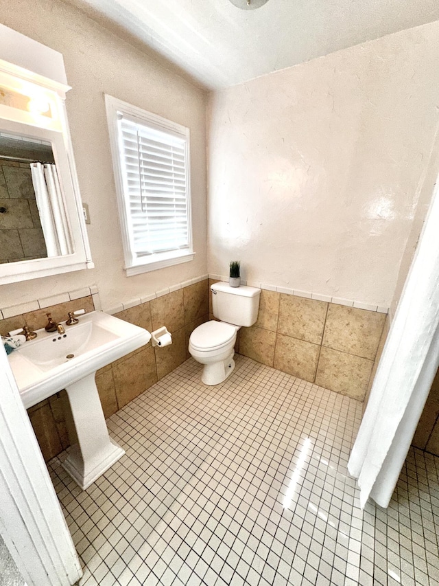 bathroom featuring toilet, wainscoting, tile walls, and tile patterned floors