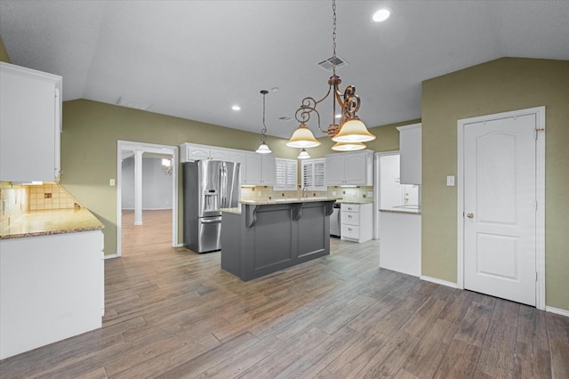 kitchen featuring vaulted ceiling, decorative light fixtures, white cabinetry, stainless steel fridge with ice dispenser, and light stone countertops