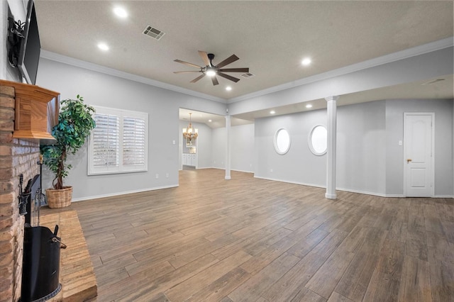 unfurnished living room with wood-type flooring, crown molding, ceiling fan with notable chandelier, and a fireplace