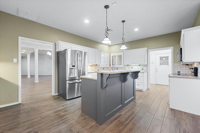 kitchen featuring light stone counters, decorative light fixtures, appliances with stainless steel finishes, a kitchen island, and white cabinets