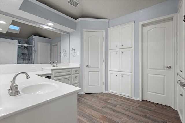 bathroom featuring a skylight, wood-type flooring, vanity, walk in shower, and a textured ceiling