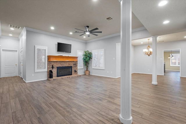 unfurnished living room with ceiling fan with notable chandelier, a fireplace, decorative columns, and light wood-type flooring