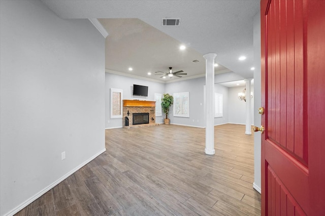 unfurnished living room with crown molding, light hardwood / wood-style flooring, a fireplace, ceiling fan with notable chandelier, and ornate columns