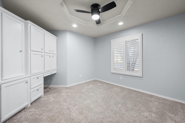 interior space with ceiling fan, a tray ceiling, built in desk, a textured ceiling, and light colored carpet