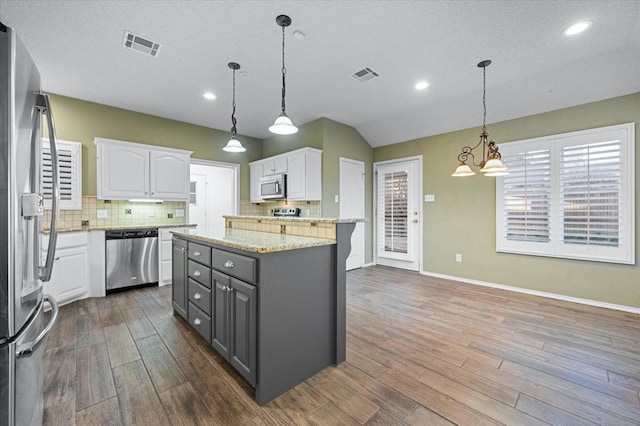 kitchen featuring gray cabinetry, white cabinetry, appliances with stainless steel finishes, pendant lighting, and light stone countertops