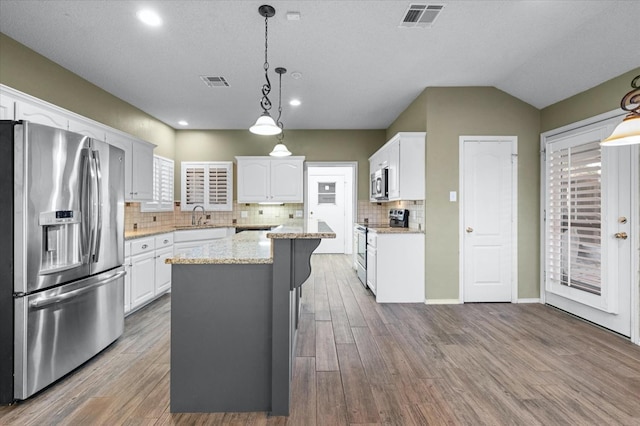 kitchen featuring a kitchen island, appliances with stainless steel finishes, decorative light fixtures, white cabinetry, and light stone countertops