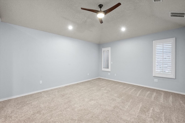 spare room featuring ceiling fan, vaulted ceiling, light carpet, and a textured ceiling