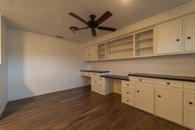 unfurnished office featuring ceiling fan, dark hardwood / wood-style floors, built in desk, and a textured ceiling