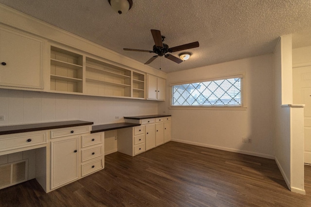 unfurnished office with ceiling fan, dark hardwood / wood-style flooring, built in desk, and a textured ceiling