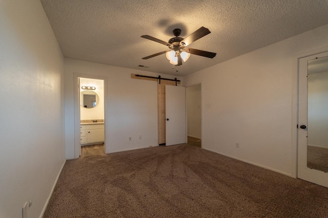 unfurnished bedroom with ensuite bathroom, a barn door, carpet floors, and a textured ceiling