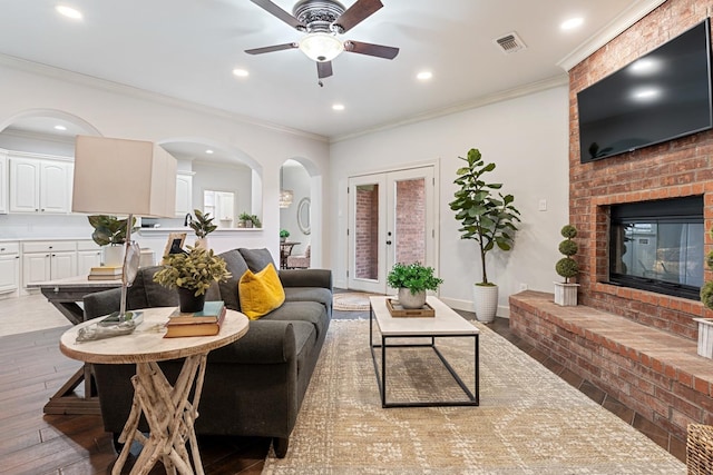 living room with a brick fireplace, ornamental molding, hardwood / wood-style floors, and ceiling fan