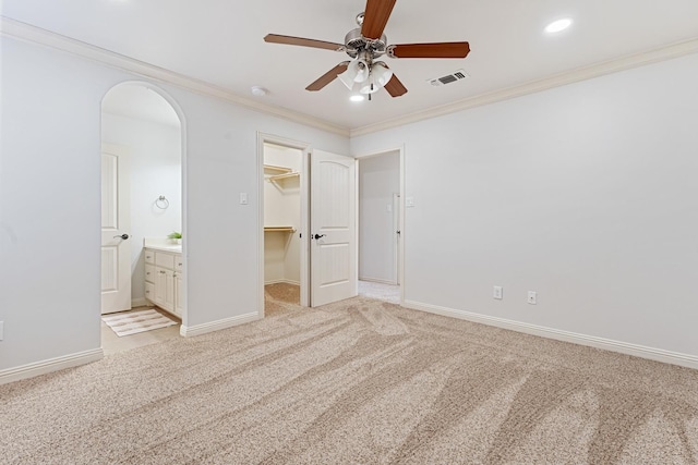 unfurnished bedroom with a walk in closet, light colored carpet, ceiling fan, crown molding, and a closet