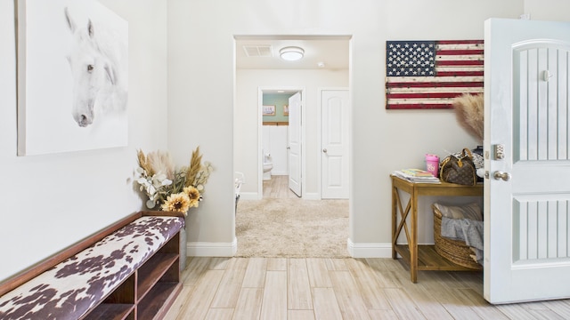 hall with baseboards, visible vents, and wood finished floors