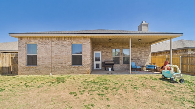 back of house featuring a patio, a chimney, a yard, brick siding, and a fenced backyard