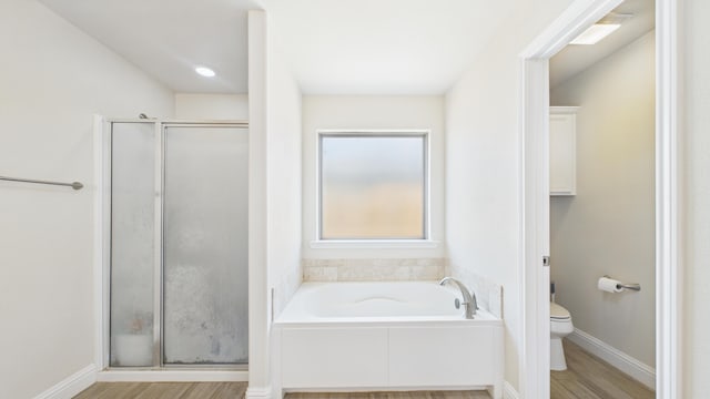 bathroom with wood finished floors, toilet, baseboards, a stall shower, and a garden tub