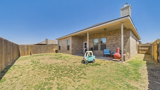 back of property with a lawn, a chimney, a fenced backyard, and brick siding